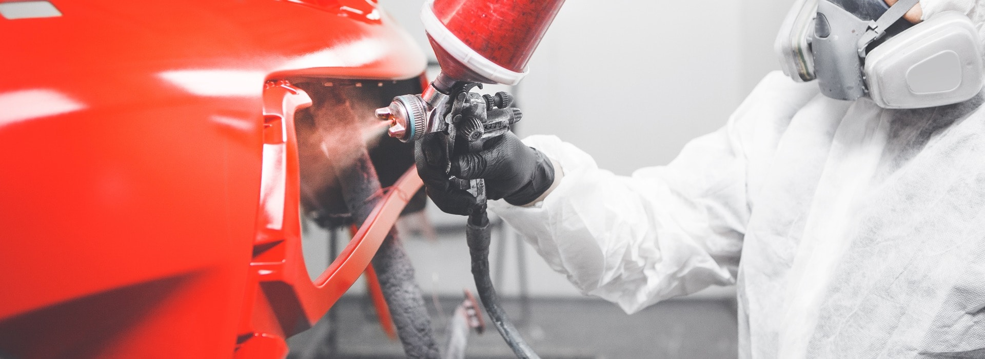 Professional male car painter is painting in garage by airbrush. Man works with spray gun.